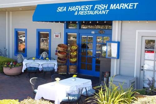 Exterior of Sea Harvest Fish Market & Restaurant, featuring outdoor seating and colorful decor under a blue awning.