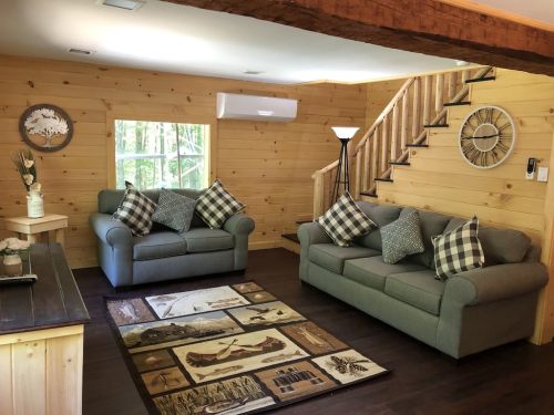 Cozy wooden living room with two sofas, decorative pillows, a rug, and a staircase in a bright, inviting space.