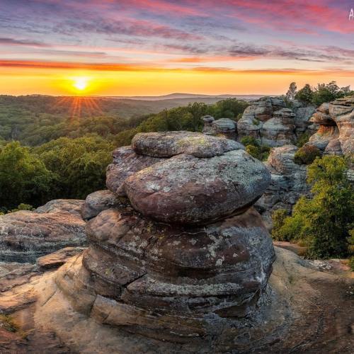 A scenic view of a sunset over rolling hills, featuring unique rock formations in the foreground.