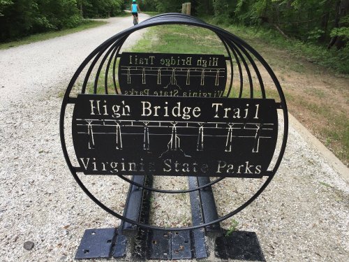 Sign for High Bridge Trail in Virginia State Parks, featuring a circular design and gravel path in the background.