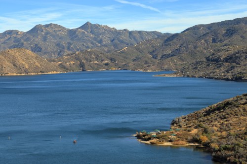 A serene lake surrounded by mountains, with clear blue water and a few boats near the shore.