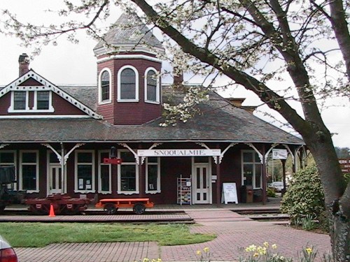 Historic Snoqualmie train station with a distinctive tower, surrounded by trees and a brick walkway.