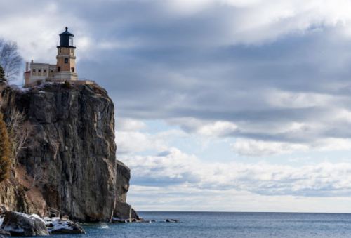 A lighthouse perched on a rocky cliff overlooking a calm sea under a cloudy sky.