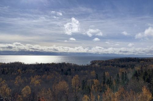 A scenic view of a lake surrounded by autumn trees under a cloudy sky.