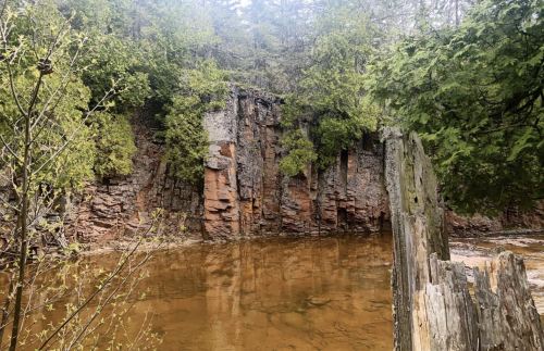 A serene river scene with rocky cliffs and lush greenery reflecting in the calm water.
