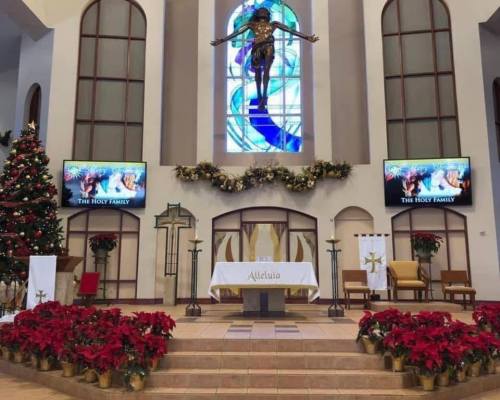 Interior of a church decorated for the holidays, featuring a large stained glass window and a nativity display.