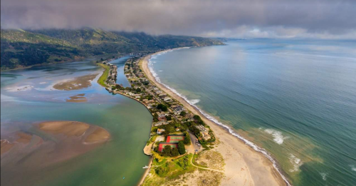 Aerial view of a coastal landscape with a winding shoreline, sandy beaches, and lush green hills in the background.