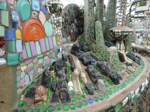 Colorful mosaic artwork featuring various materials, including glass, stones, and ceramics, creating a vibrant landscape.
