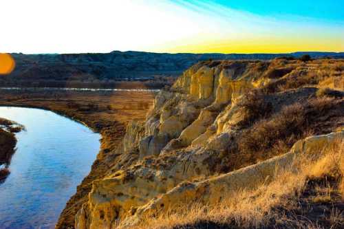 A scenic view of yellowish cliffs beside a calm river, with a vibrant sunset sky in the background.