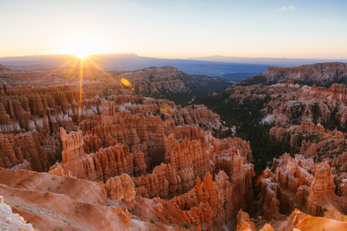 Sunrise over Bryce Canyon, highlighting the orange rock formations and layered cliffs in a serene landscape.
