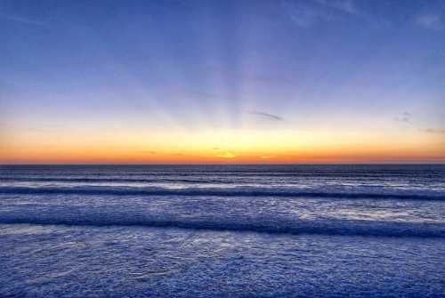 A serene ocean view at sunset, with vibrant colors and rays of light illuminating the horizon.