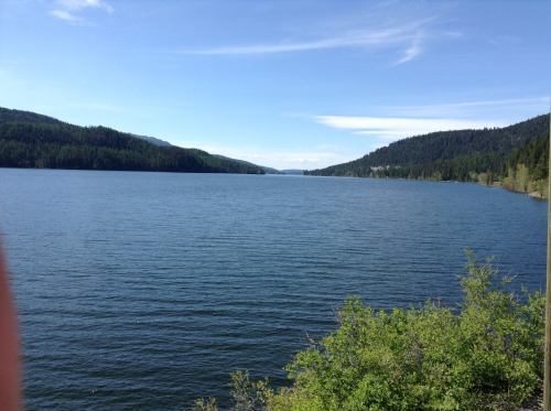A serene lake surrounded by green hills under a clear blue sky, with calm water reflecting the landscape.