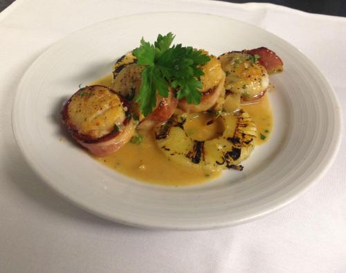 A plate of scallops wrapped in bacon, served with grilled pineapple and a light sauce, garnished with parsley.
