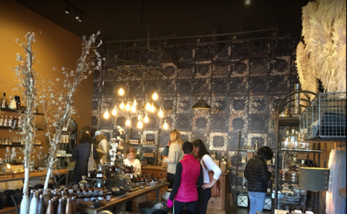 A cozy shop interior with people browsing, featuring decorative lights, shelves of bottles, and a patterned wall.