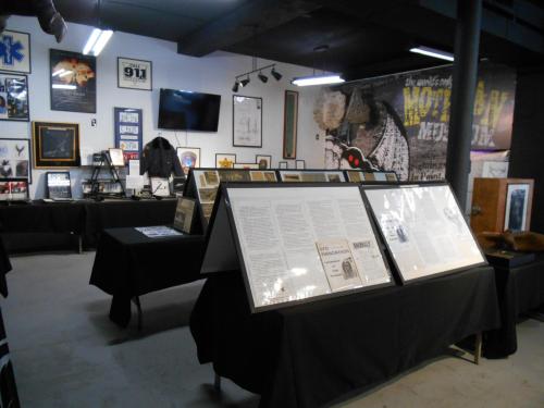 A gallery space featuring framed artworks, displays, and informational panels on black tables.