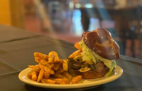 A delicious burger on a pretzel bun with lettuce, served with seasoned sweet potato fries on a plate.