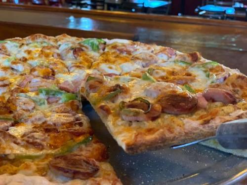 A close-up of a pizza with toppings like green peppers, ham, and cheese, with a slice being lifted from the pie.