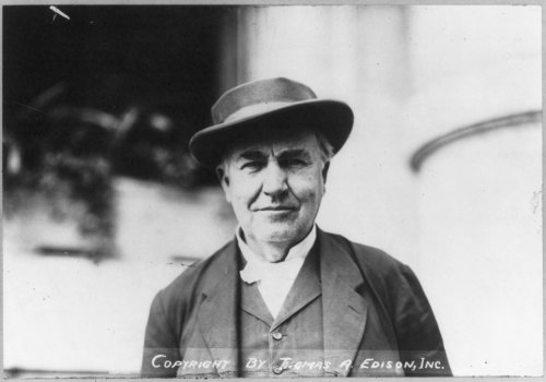 A historical black-and-white portrait of a man wearing a hat and suit, smiling at the camera.