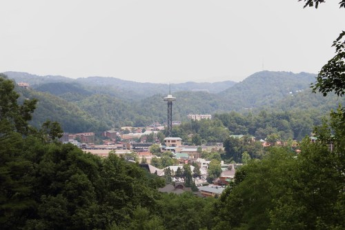 A scenic view of a town surrounded by green mountains, featuring a tall observation tower in the distance.