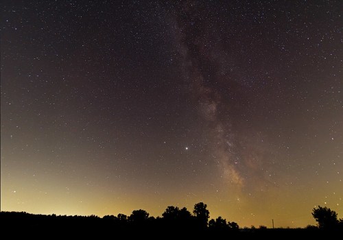 A starry night sky featuring the Milky Way, with silhouettes of trees against a glowing horizon.