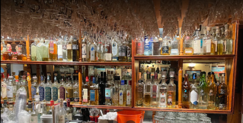 A well-stocked bar with various bottles of liquor displayed on shelves and glasses hanging overhead.