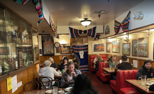 A cozy restaurant interior with colorful decorations, featuring diners at booths and tables enjoying their meals.