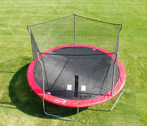A round trampoline with a red border and black safety net, set on a grassy field.