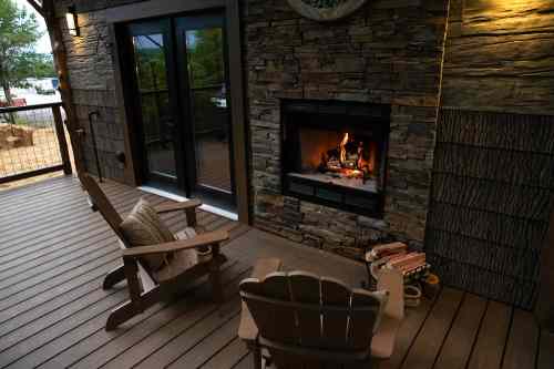 Cozy outdoor space with two chairs, a stone fireplace, and double doors leading to a serene setting.