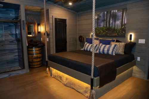 Cozy bedroom with a suspended bed, wooden accents, and soft lighting, featuring a nature-themed painting on the wall.