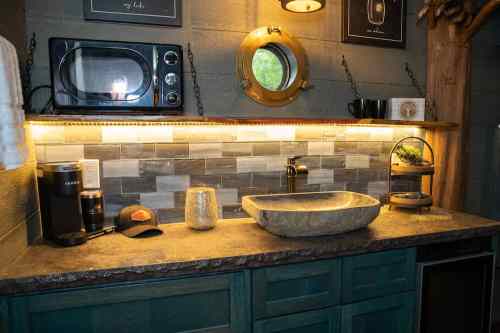 A cozy kitchen with a stone sink, coffee maker, and vintage decor, featuring warm lighting and a rustic vibe.