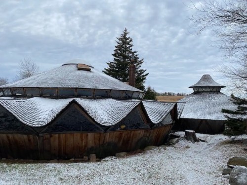 Two unique, dome-shaped buildings with snow-covered roofs, surrounded by trees and a cloudy sky.