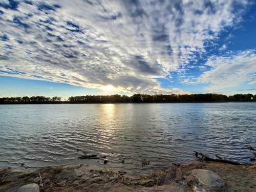 A serene river scene at sunset, with clouds reflecting in the water and trees lining the opposite shore.