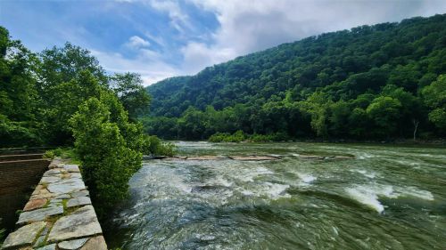 A scenic river flows through a lush green landscape, with hills and trees under a partly cloudy sky.