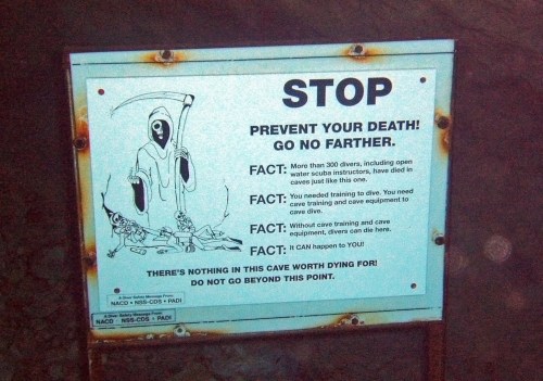 Sign warning against entering a cave without proper training and equipment, emphasizing safety and potential dangers.