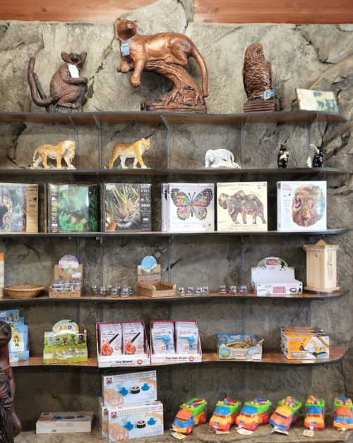 A display shelf featuring wooden animal carvings, puzzles, and various toys in a rustic setting.