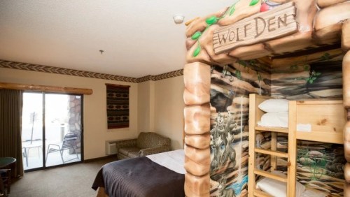 A cozy hotel room featuring a unique bunk bed with a "Wolf Den" theme and a seating area by a balcony.