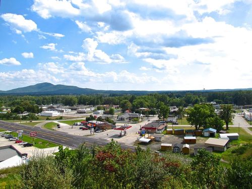 A scenic view of a small town with shops, roads, and mountains under a partly cloudy sky.