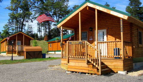Two wooden cabins with porches, surrounded by trees, and an American flag waving in the breeze.