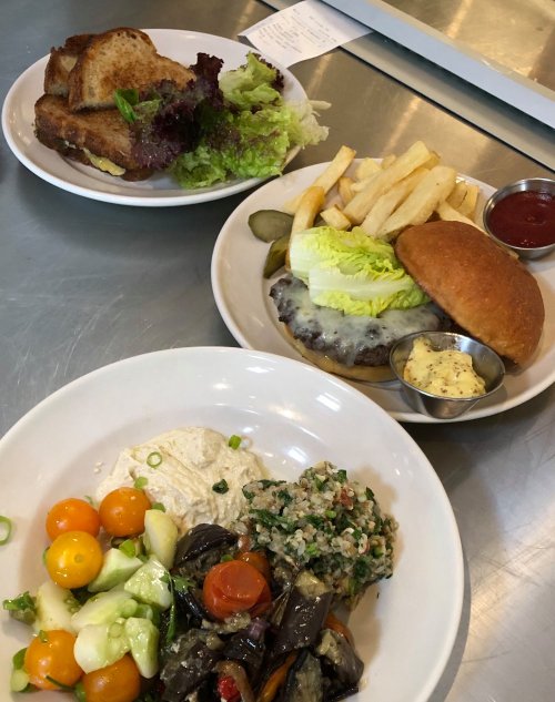 A plate with a burger, fries, and pickles; a salad; and a bowl of hummus with assorted vegetables and grains.