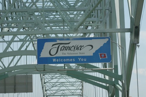 Sign welcoming visitors to Tennessee, featuring the state outline and flag, displayed on a bridge structure.