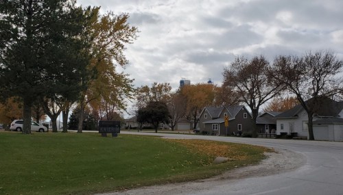 A quiet neighborhood with trees and houses, featuring a curved road and cloudy skies in the background.