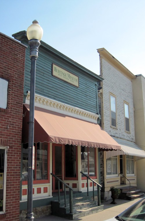 A blue building with a sign reading "Heritage Museum," featuring a brown awning and a lamp post in front.