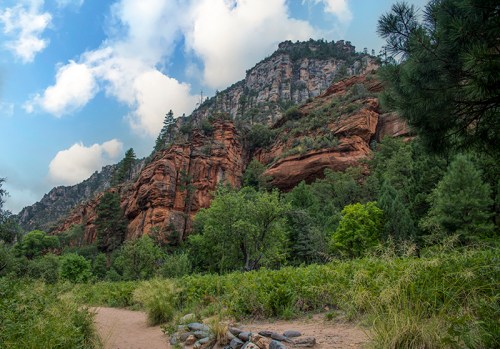 A scenic view of red rock formations and lush greenery under a partly cloudy sky.