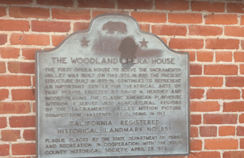 Plaque detailing the history of the Woodland Opera House, a California historical landmark, against a brick wall.