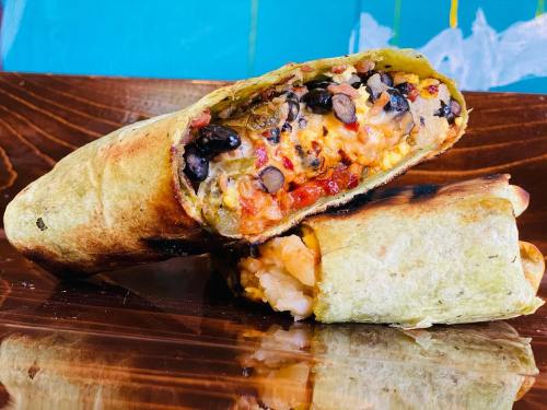 A close-up of a cut burrito filled with beans, cheese, and rice, resting on a wooden plate.
