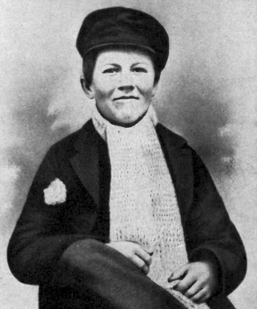 A historical black-and-white portrait of a young person wearing a hat and a knitted scarf, seated with a slight smile.