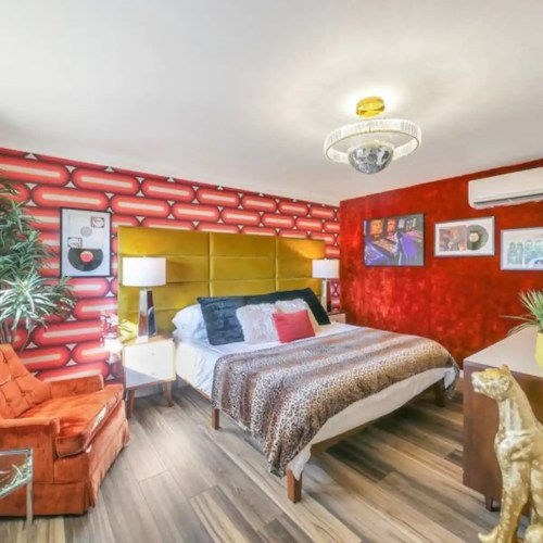 A vibrant bedroom featuring a red accent wall, leopard print bedding, and retro decor with a cozy seating area.