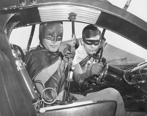 Batman and Robin sit in the Batmobile, ready for action, dressed in their iconic superhero costumes.