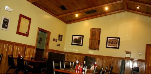 Cozy restaurant interior with wooden walls, framed photos, and tables set with condiments. Warm lighting enhances the ambiance.