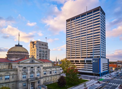 Cityscape featuring a historic building and a modern high-rise against a colorful sky.